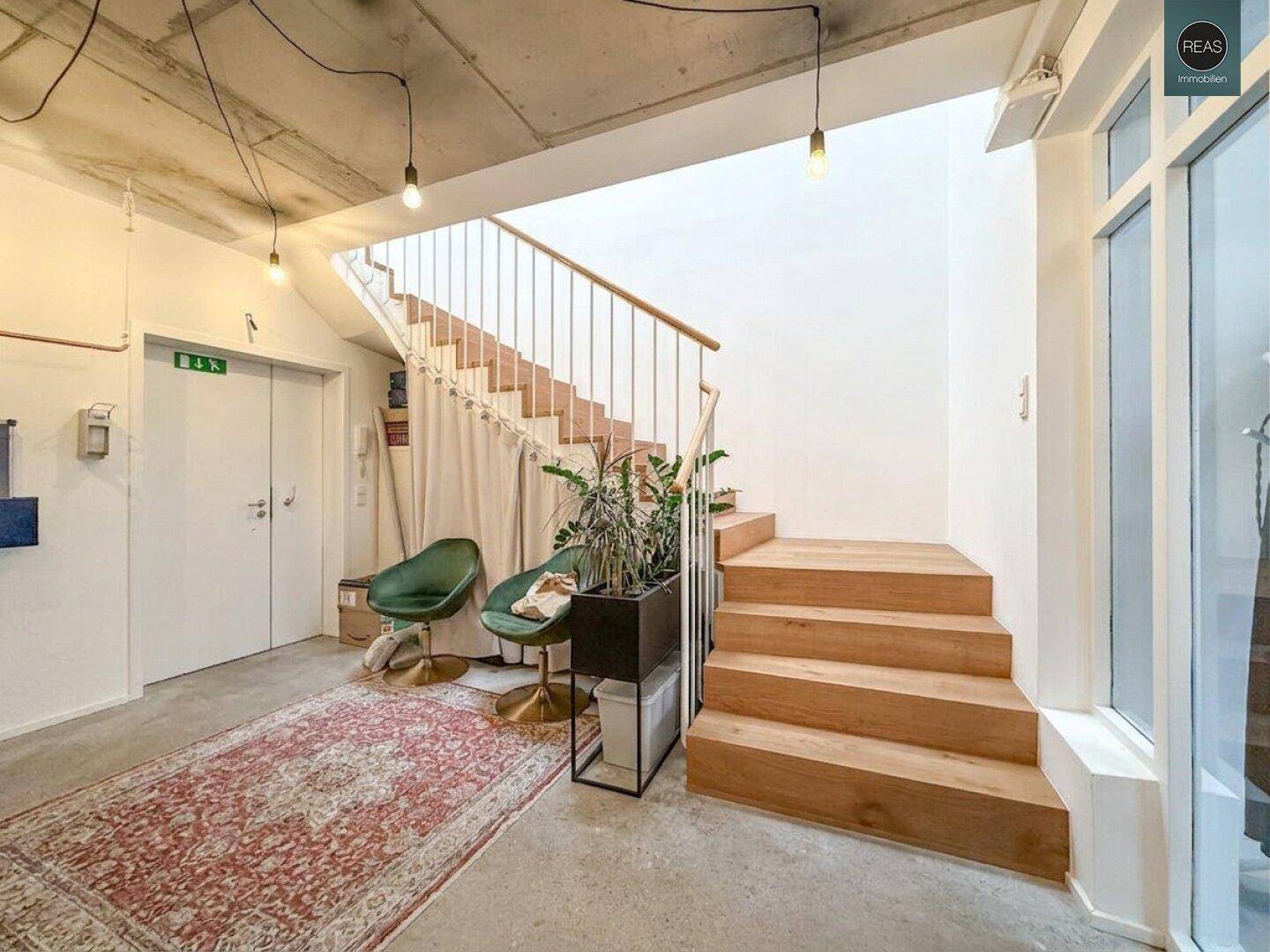 Eingangsbereich mit Holztreppe, Betonboden und einem dekorativen Teppich.