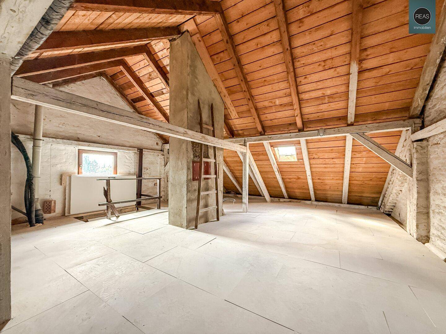 Ausbaufähiger Dachboden mit sichtbarer Holzkonstruktion und kleinen Fenstern für Tageslicht.