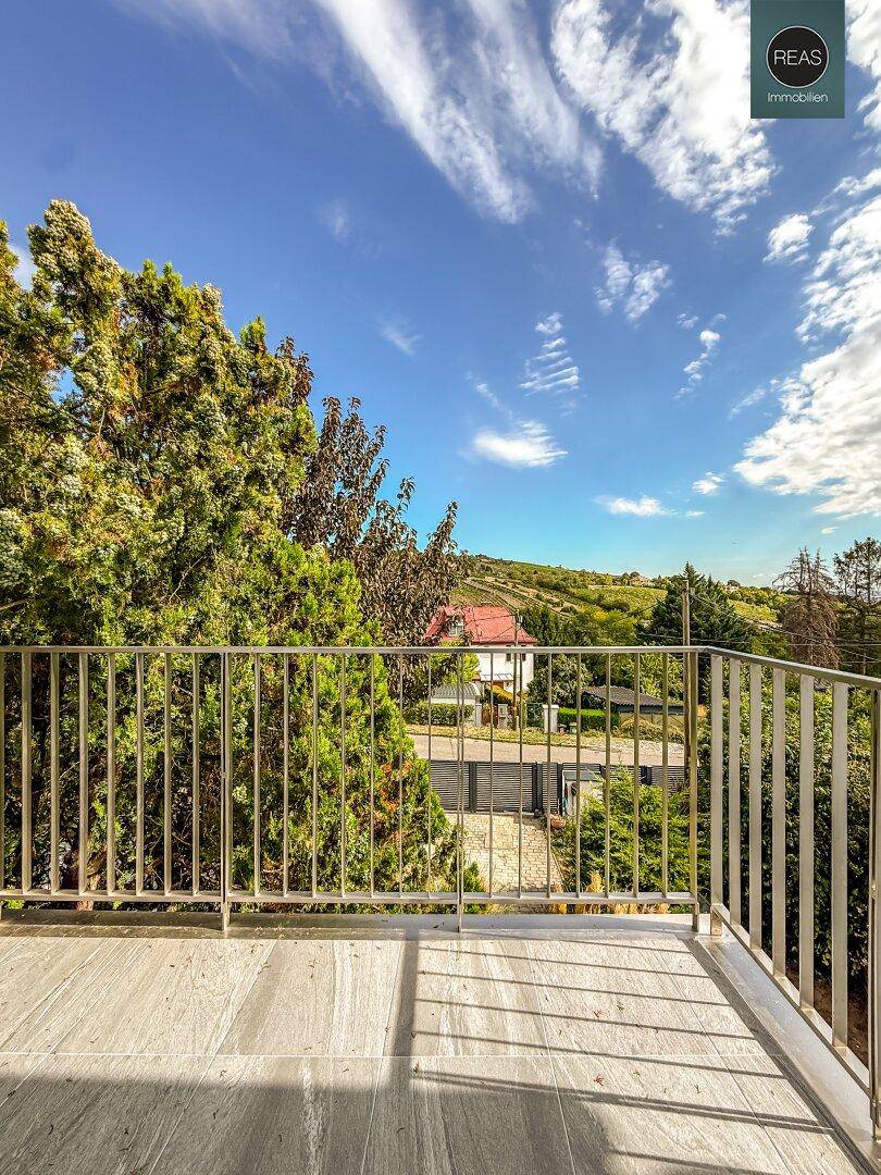 Geräumiger Balkon mit Metallgeländer und weitem Blick über die grüne Landschaft unter blauem Himmel.