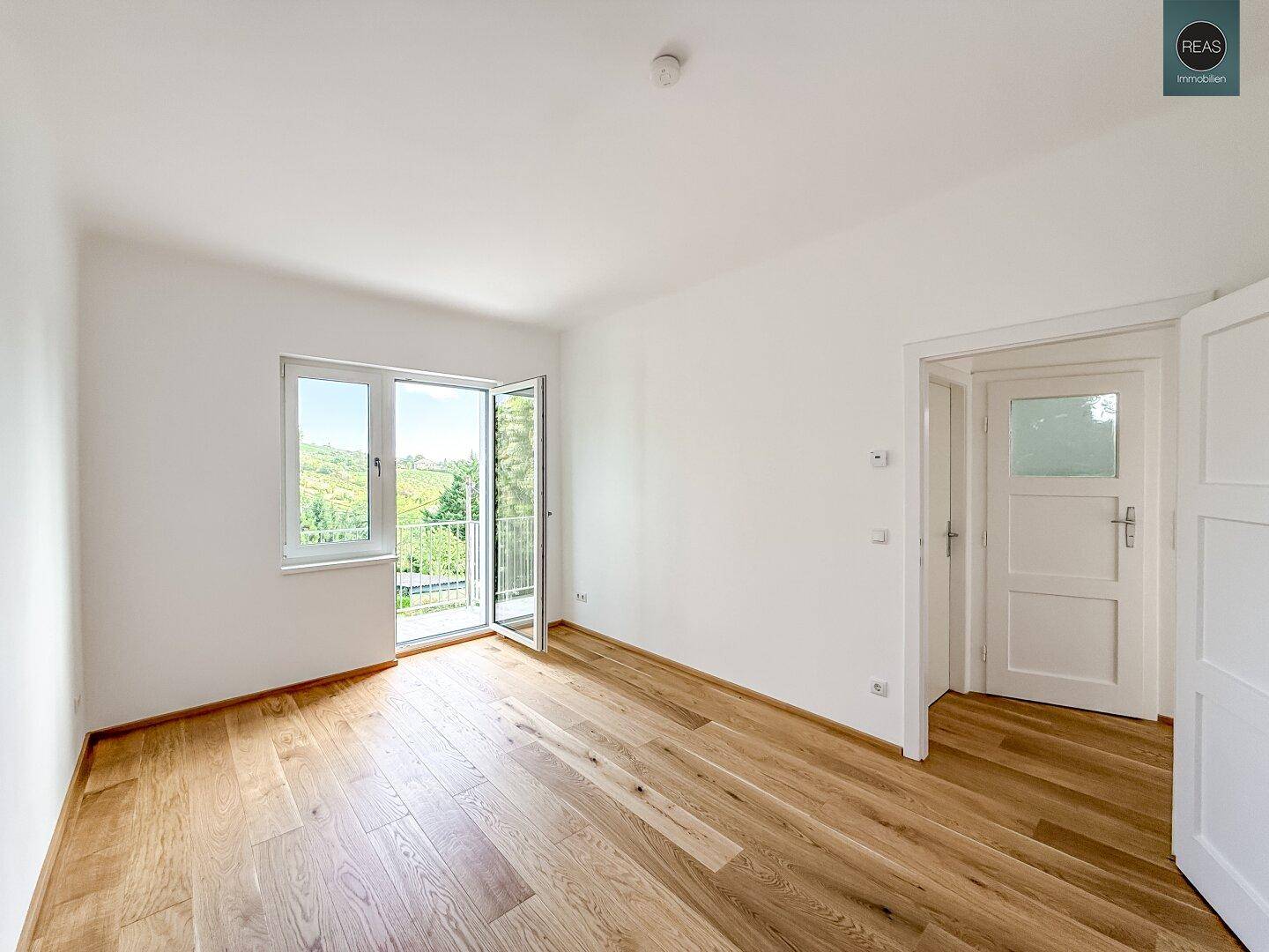 Helles Zimmer mit Eichenparkettboden und Zugang zu einem Balkon mit schöner Aussicht.