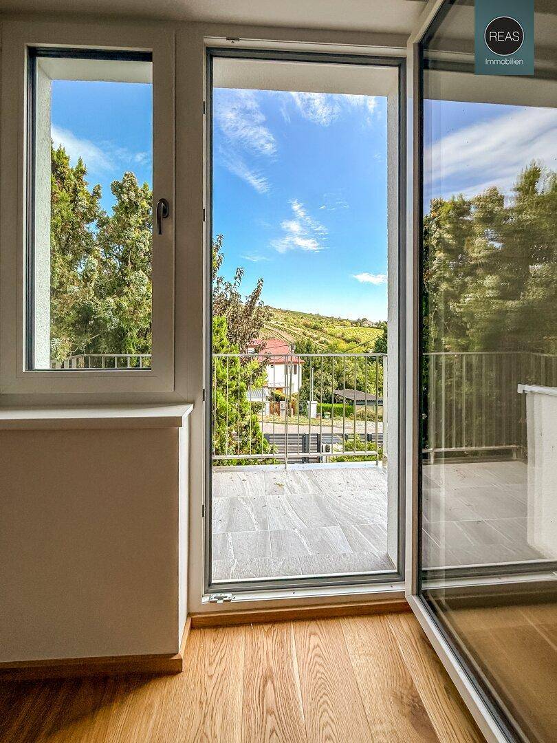 Blick vom Zimmer auf einen Balkon mit Fliesenboden und weitreichender grüner Aussicht.