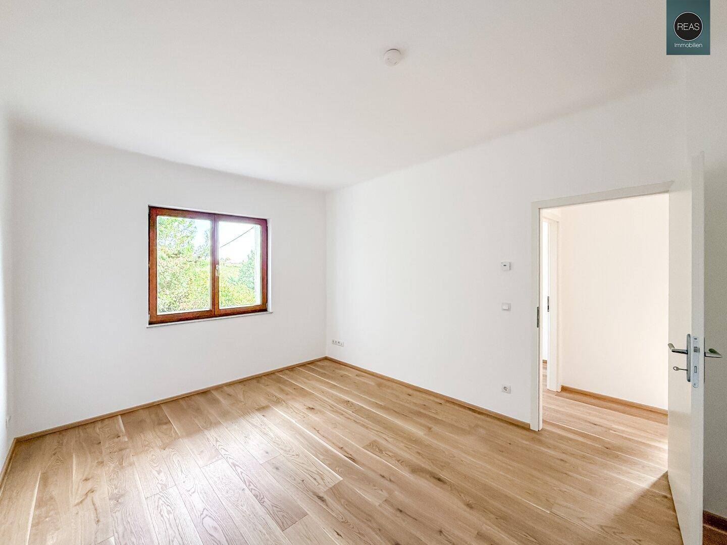 Helles Schlafzimmer mit Holzboden und Fenster mit Blick ins Grüne.