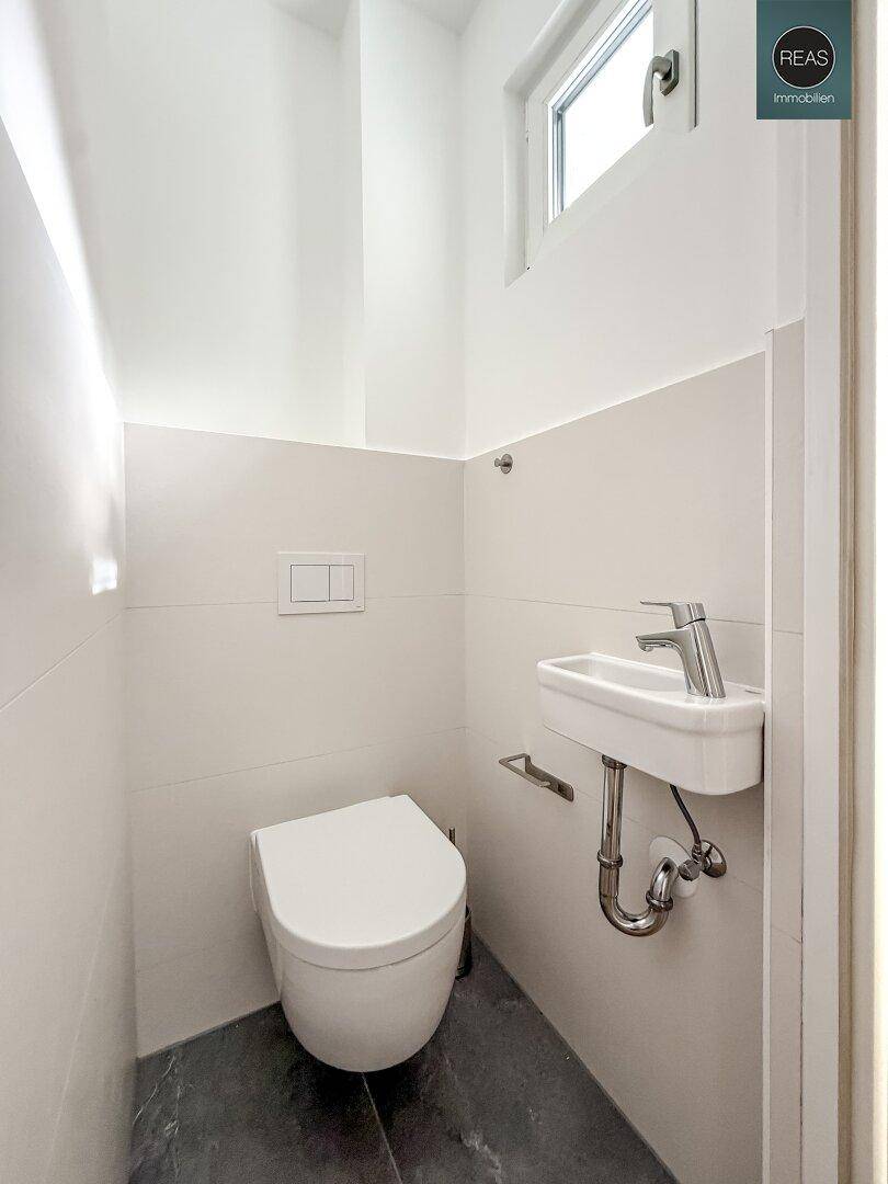 Modernes Gäste-WC mit wandhängendem WC, kleinem Waschbecken und Fenster für Tageslicht.