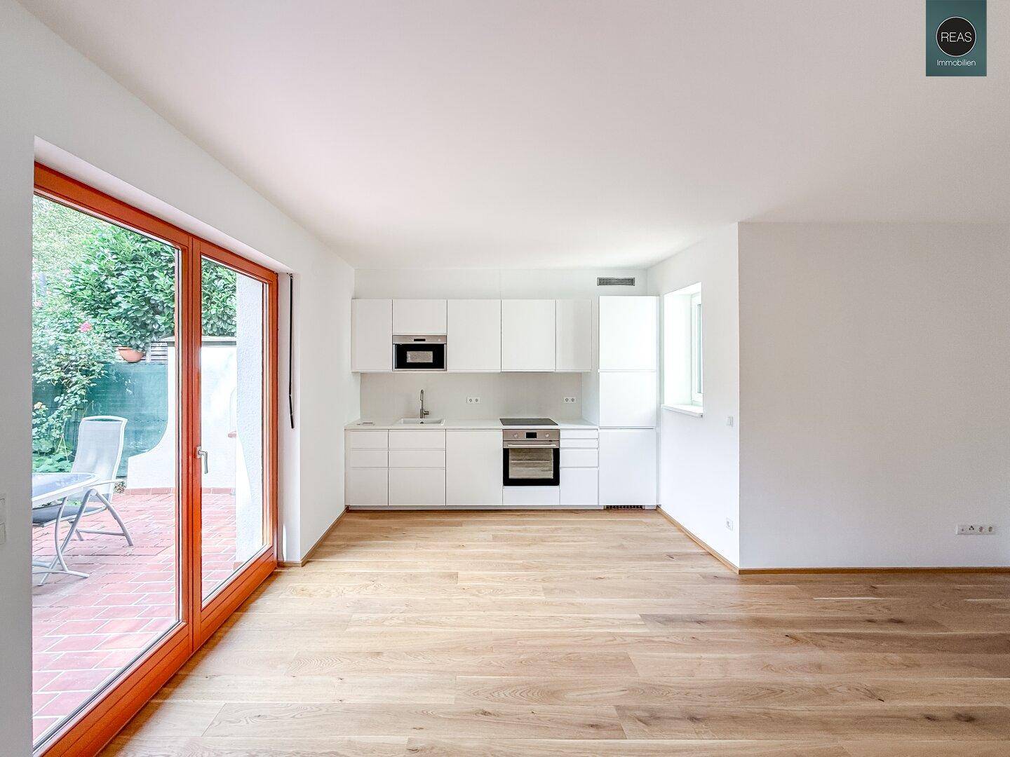 Offener Wohnbereich mit Küchenzeile, Holzboden und Zugang zur Terrasse.