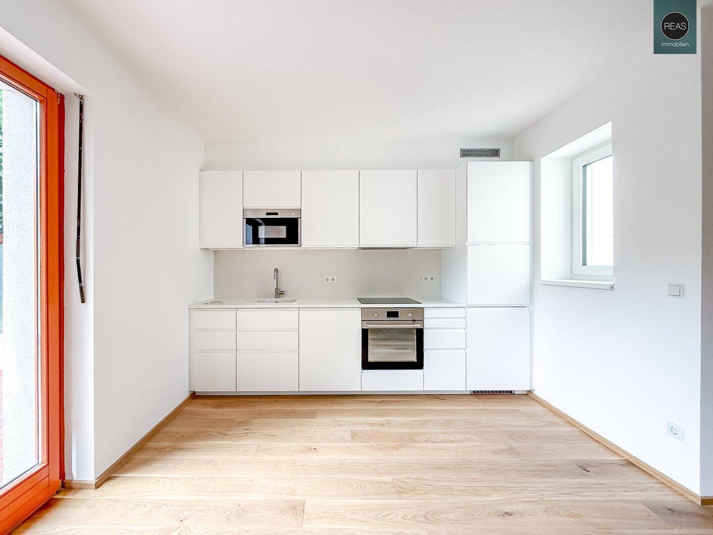 Moderne weiße Küchenzeile mit integrierten Geräten und Fenster.