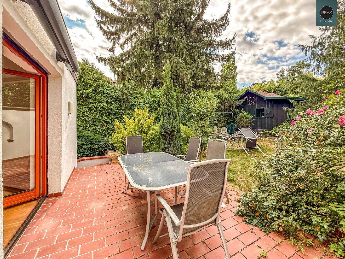 Geräumige Terrasse mit Gartenmöbeln und Blick auf den Garten mit Gartenhaus.