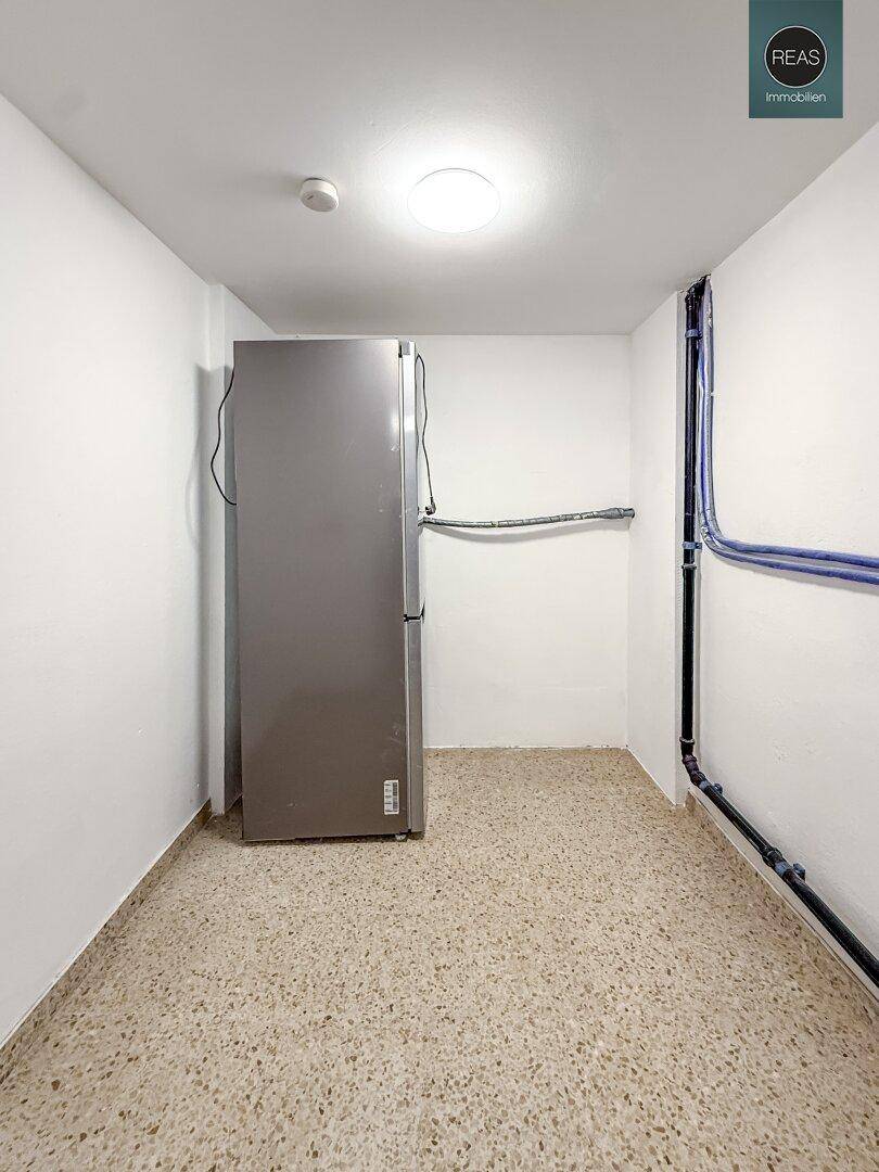 Kellerraum mit einem großen Kühlschrank und sichtbaren Installationen an der Wand.