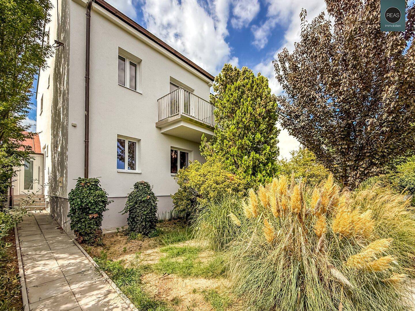 Seitenansicht des weißen Wohnhauses mit kleinem Balkon und grüner Umgebung.