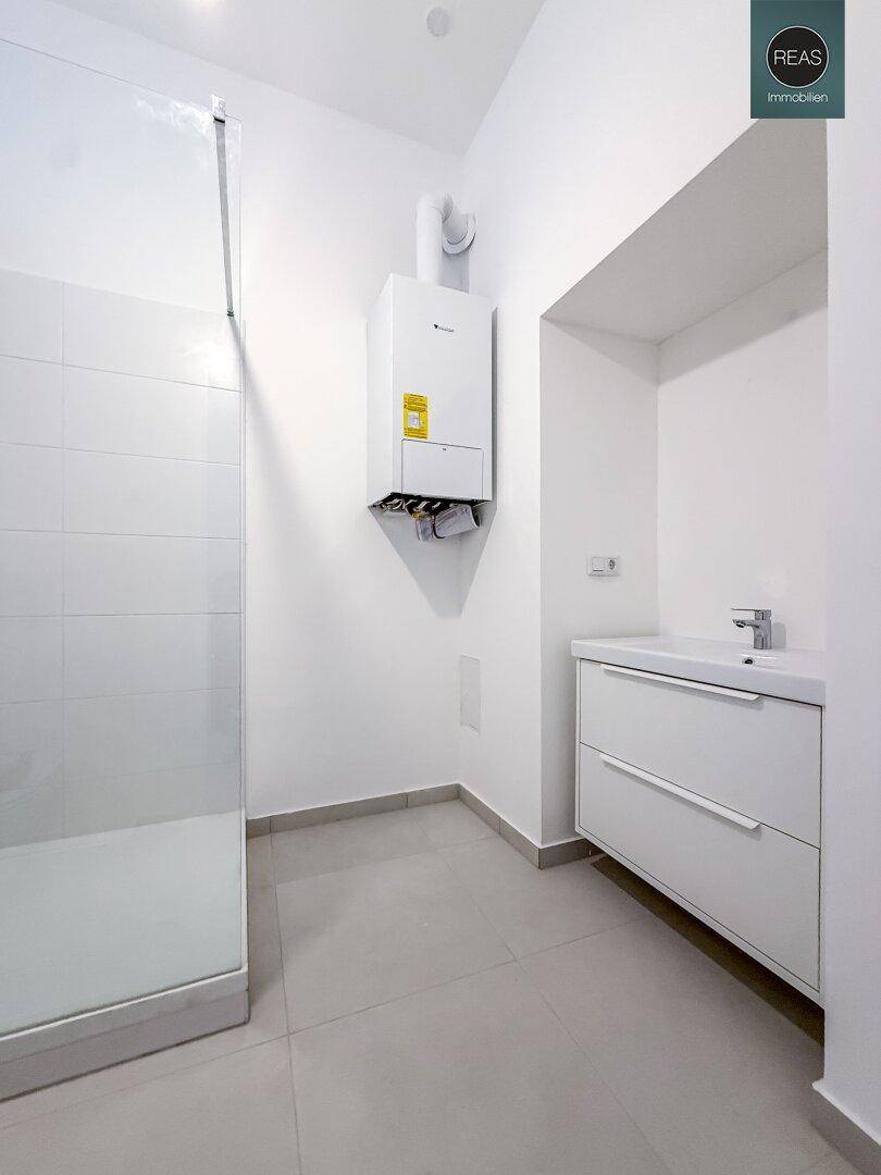 Modernes Badezimmer mit Duschkabine, Waschbeckenunterschrank und Warmwasserbereiter an der Wand.