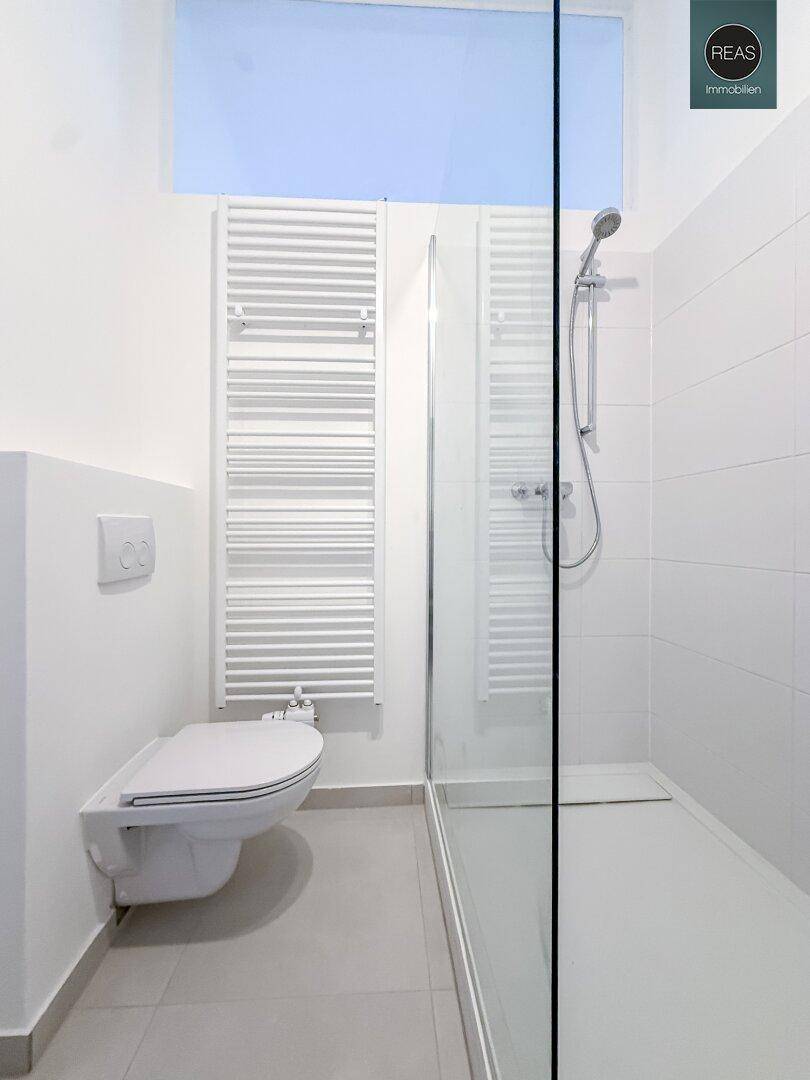 Helles Badezimmer mit wandhängendem WC, Duschbereich und Handtuchheizkörper, modern gestaltet.