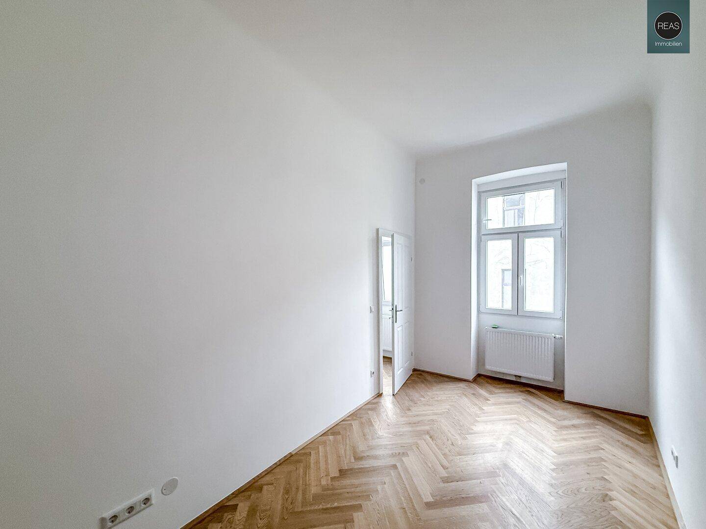 Ein weiterer heller Raum mit Fischgrätparkett und einem großen Fenster, das den Raum erhellt.