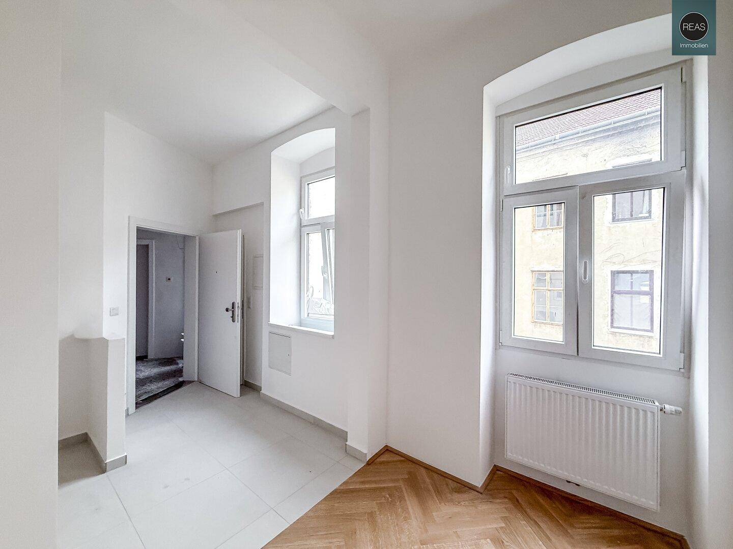 Flur mit Fliesenboden, der zu einem Raum mit Parkett und einem Fenster führt, hell und einladend.