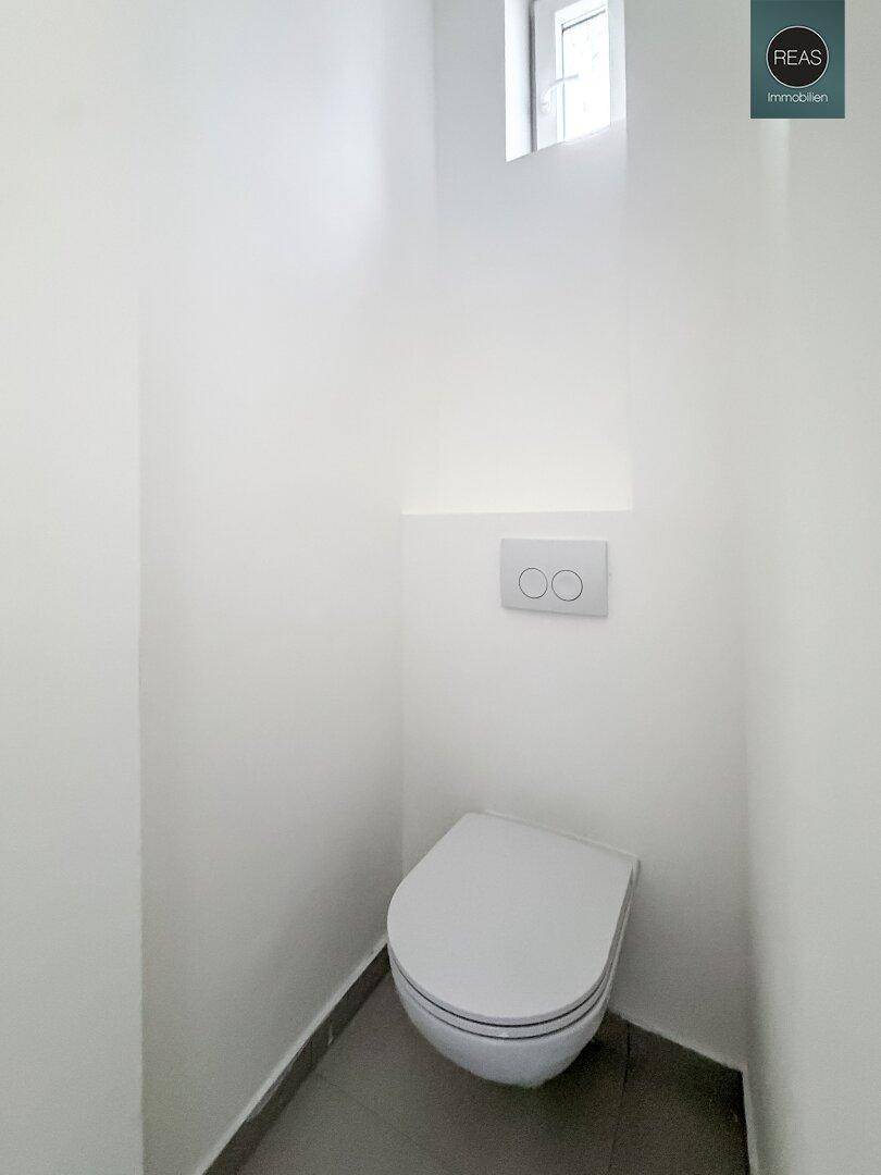 Kompaktes Gäste-WC mit wandhängender Toilette und kleinem Fenster für natürliche Belüftung.