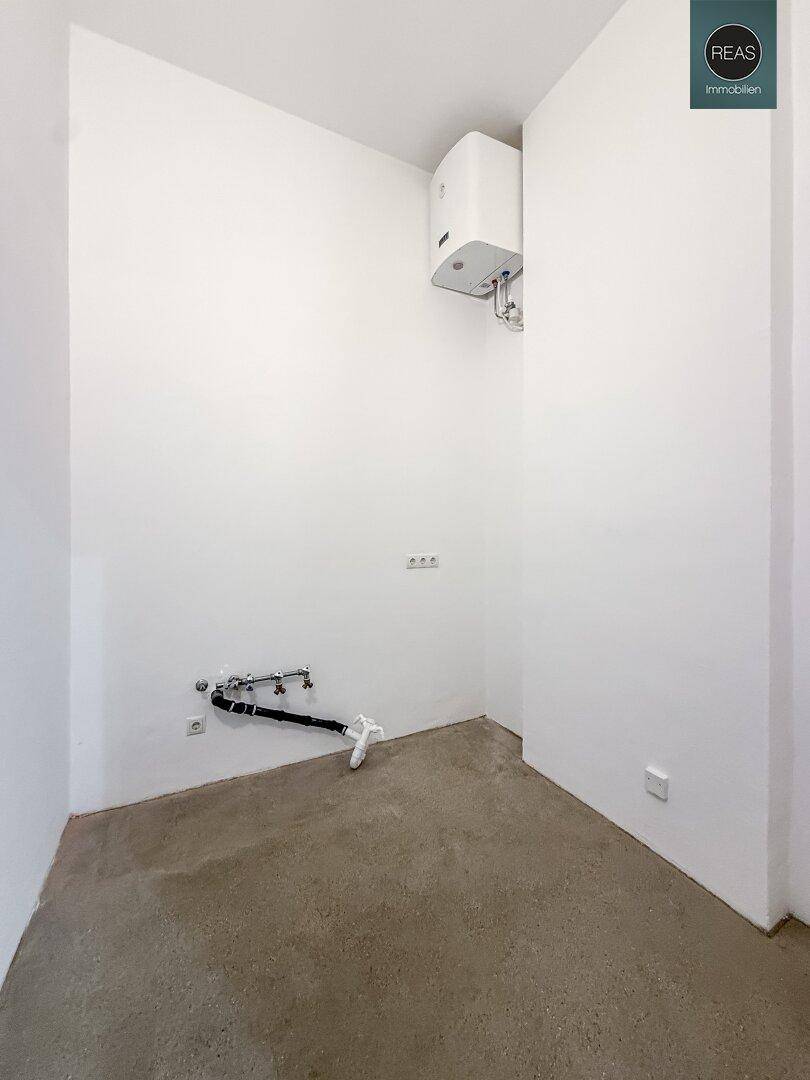 Kleiner Raum mit Warmwasserbereiter und Anschlüssen für eine Waschmaschine, ideal als Hauswirtschaftsraum.