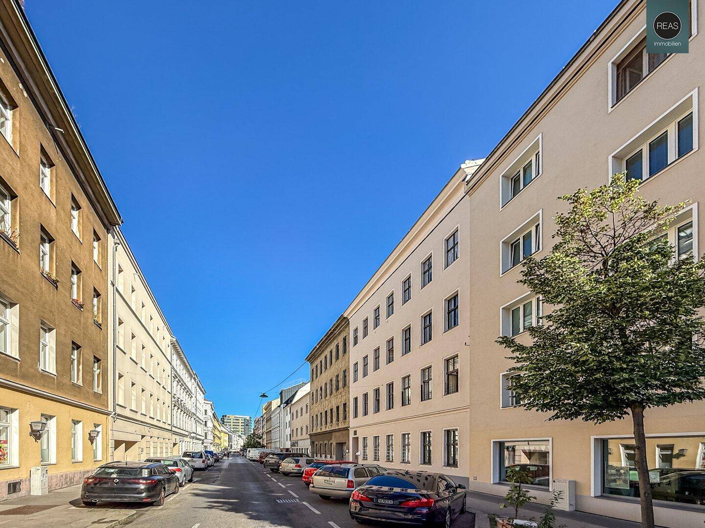 Eine ruhige Wohnstraße mit geparkten Autos und mehrstöckigen Gebäuden unter einem klaren blauen Himmel.