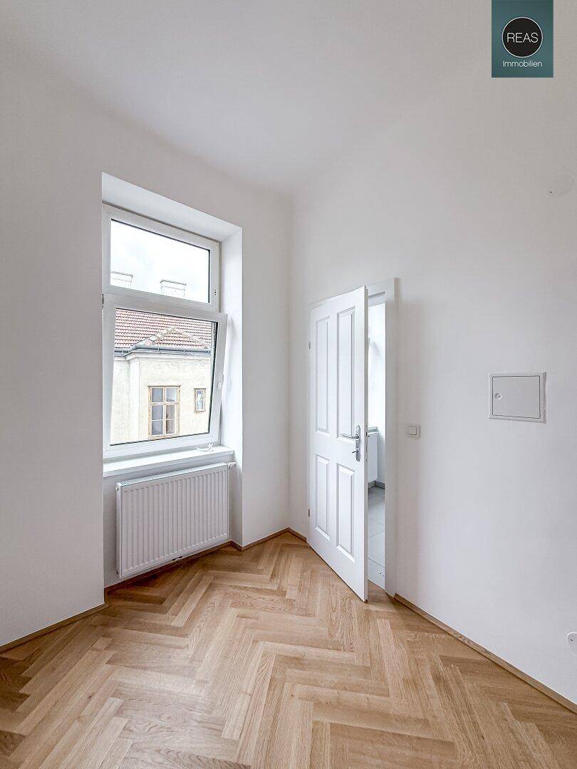 Freundlicher Raum mit Fischgrätparkett und einem Fenster, das Tageslicht hereinlässt, bereit zur Einrichtung.