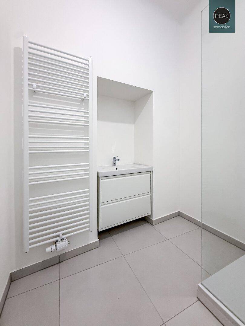 Modernes Badezimmer mit grauen Fliesen, einem Handtuchheizkörper und einem stilvollen Waschtischunterschrank.