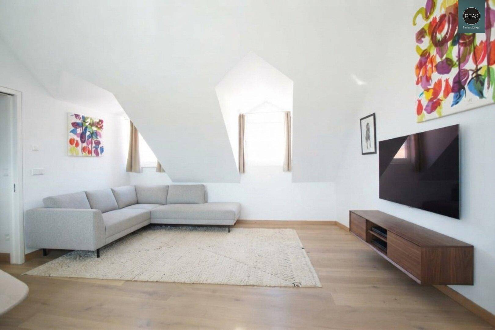 Geräumiges Wohnzimmer im Dachgeschoss mit Dachschrägen, Ecksofa und Holzboden.