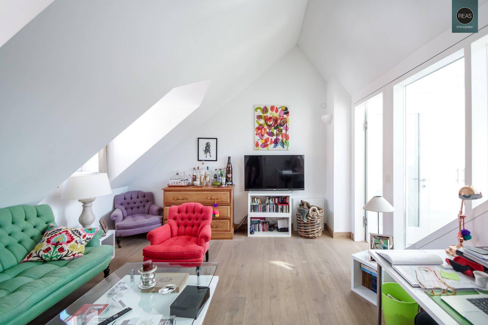 Gemütliches Wohnzimmer im Dachgeschoss mit bunten Möbeln, Dachschrägen und Holzboden.