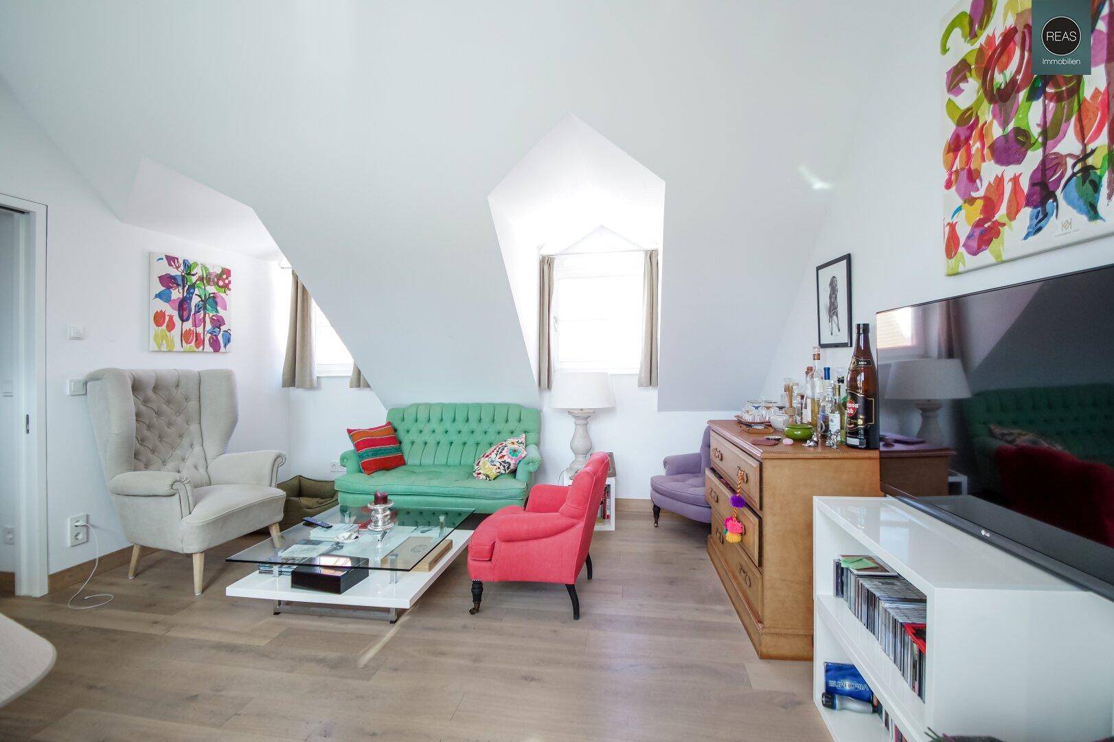 Helles Wohnzimmer im Dachgeschoss mit bunten Möbeln, Dachschrägen und Holzboden.