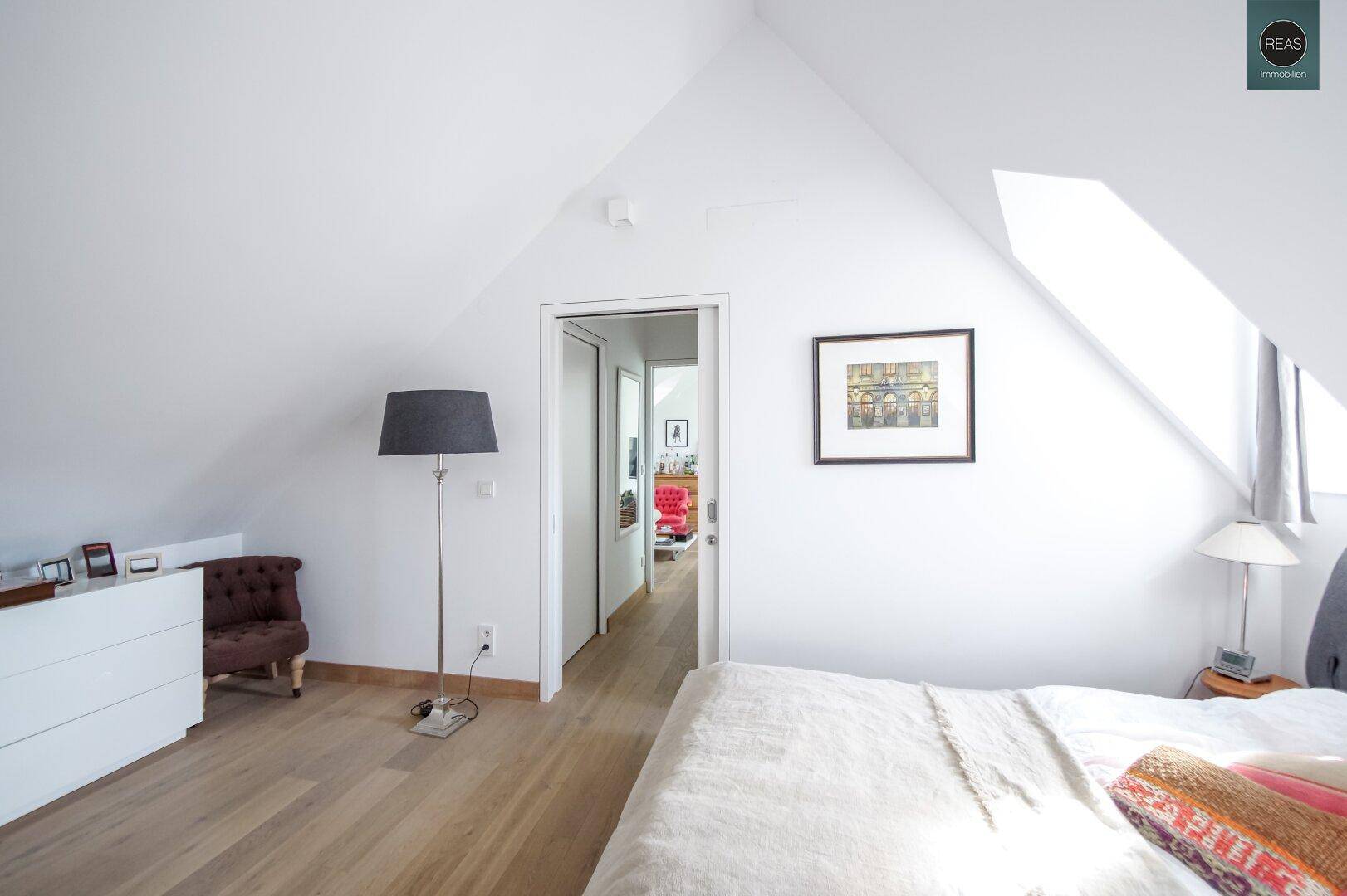 Schlafzimmer im Dachgeschoss mit Dachschrägen, Holzboden und Zugang zum Flur.