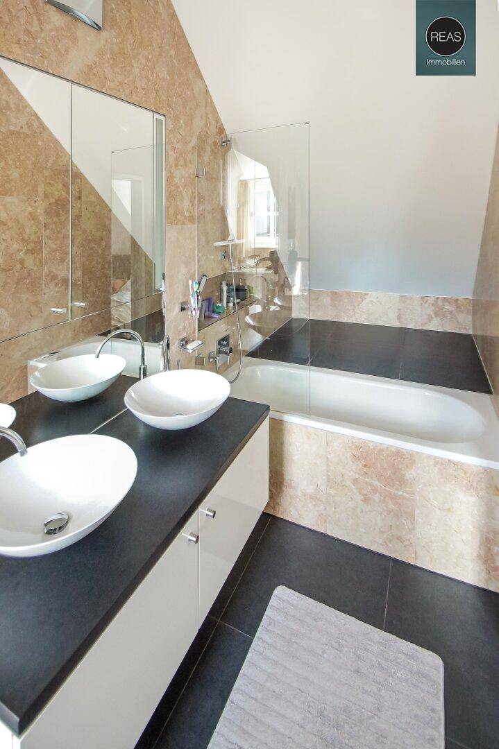 Modernes Badezimmer mit Doppelwaschbecken, Badewanne und eleganten Fliesen.