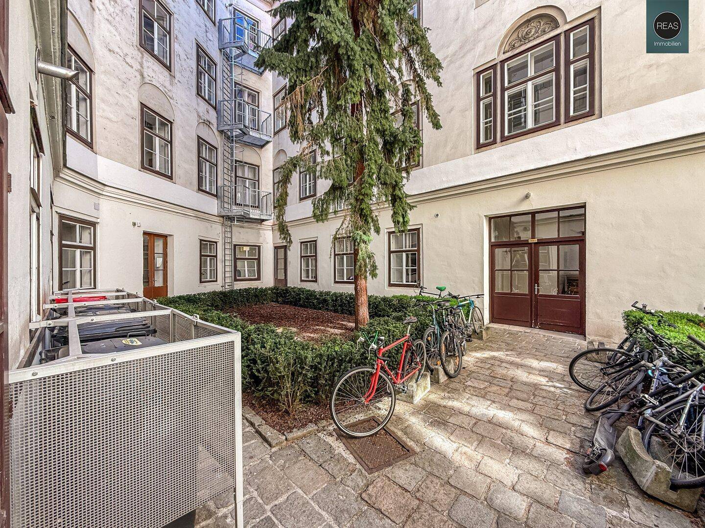 Innenhof eines Altbaus mit Bäumen, Sträuchern und abgestellten Fahrrädern.