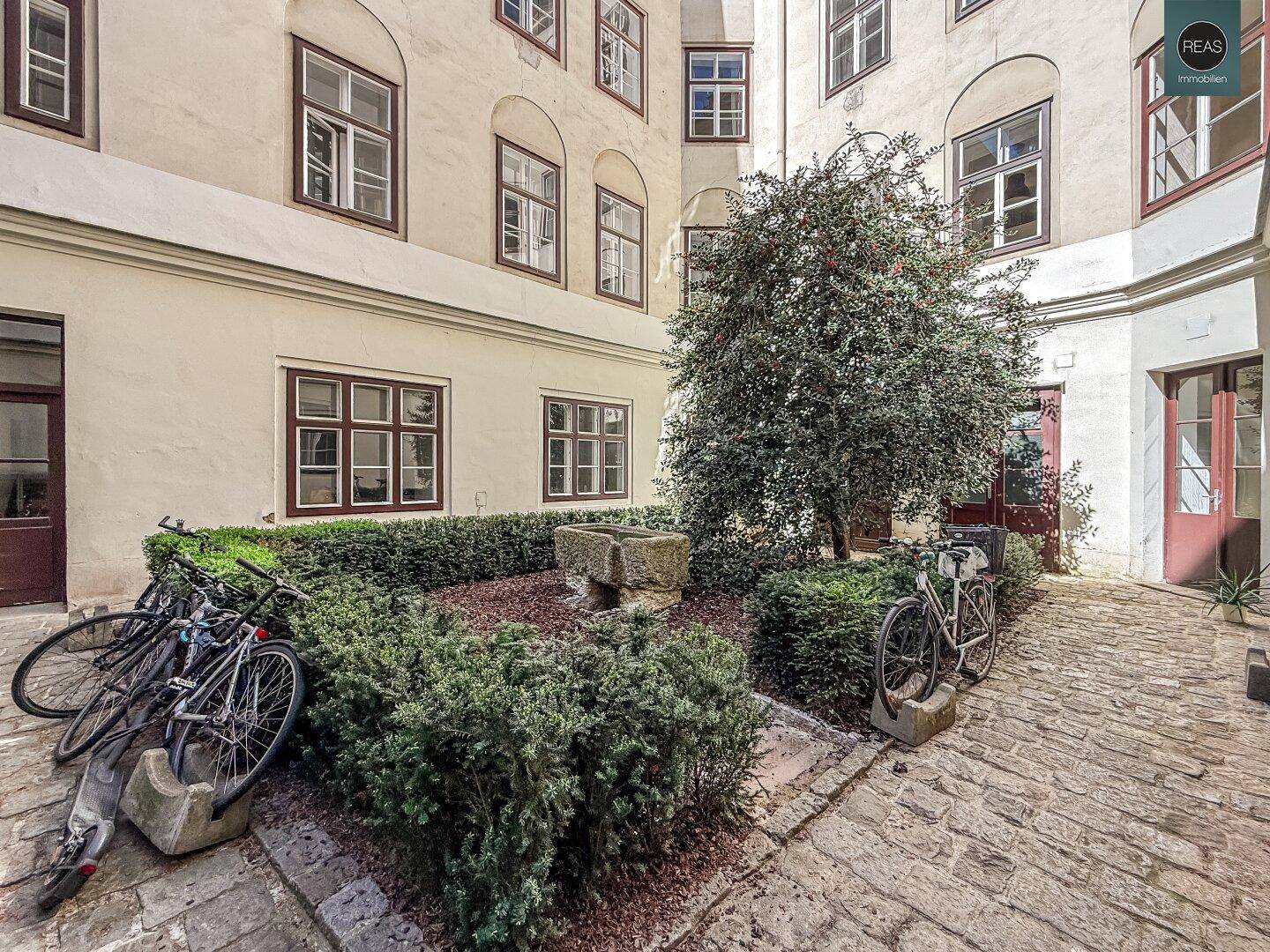Gepflegter Innenhof mit Kopfsteinpflaster, Grünflächen und einem alten Steinbrunnen.