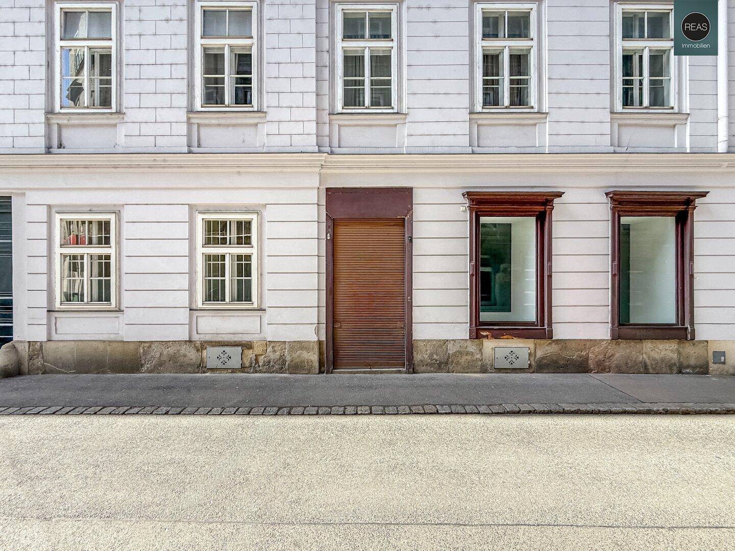 Historische Fassade eines Gebäudes mit mehreren Fenstern und einem Holztor zur Straße hin.