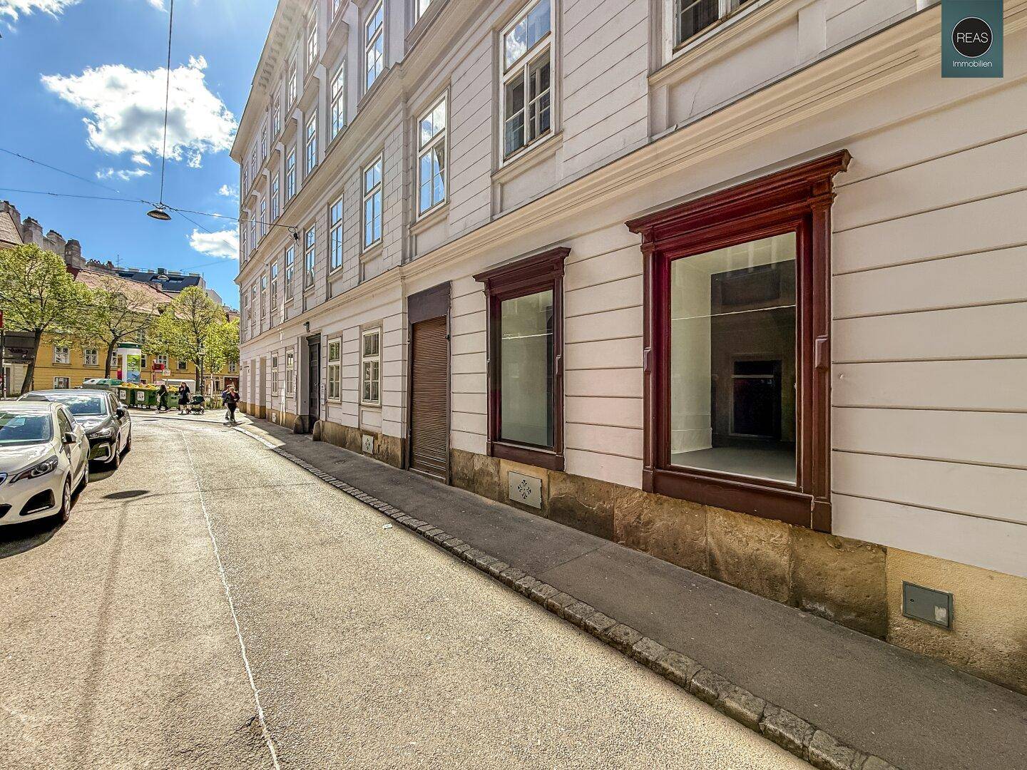 Seitenansicht eines historischen Gebäudes an einer sonnigen Straße mit parkenden Autos.