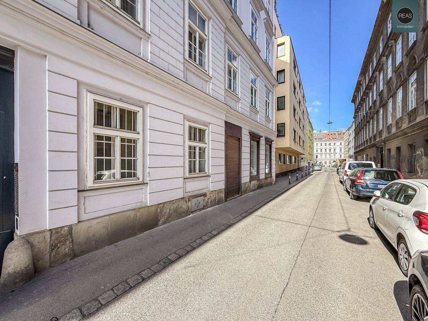Lange Straße mit historischen Gebäuden und modernen Elementen unter blauem Himmel.