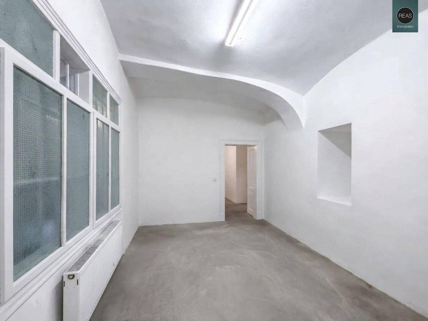Heller Raum mit gewölbter Decke, großen Fenstern und einem Heizkörper unter dem Fenster.