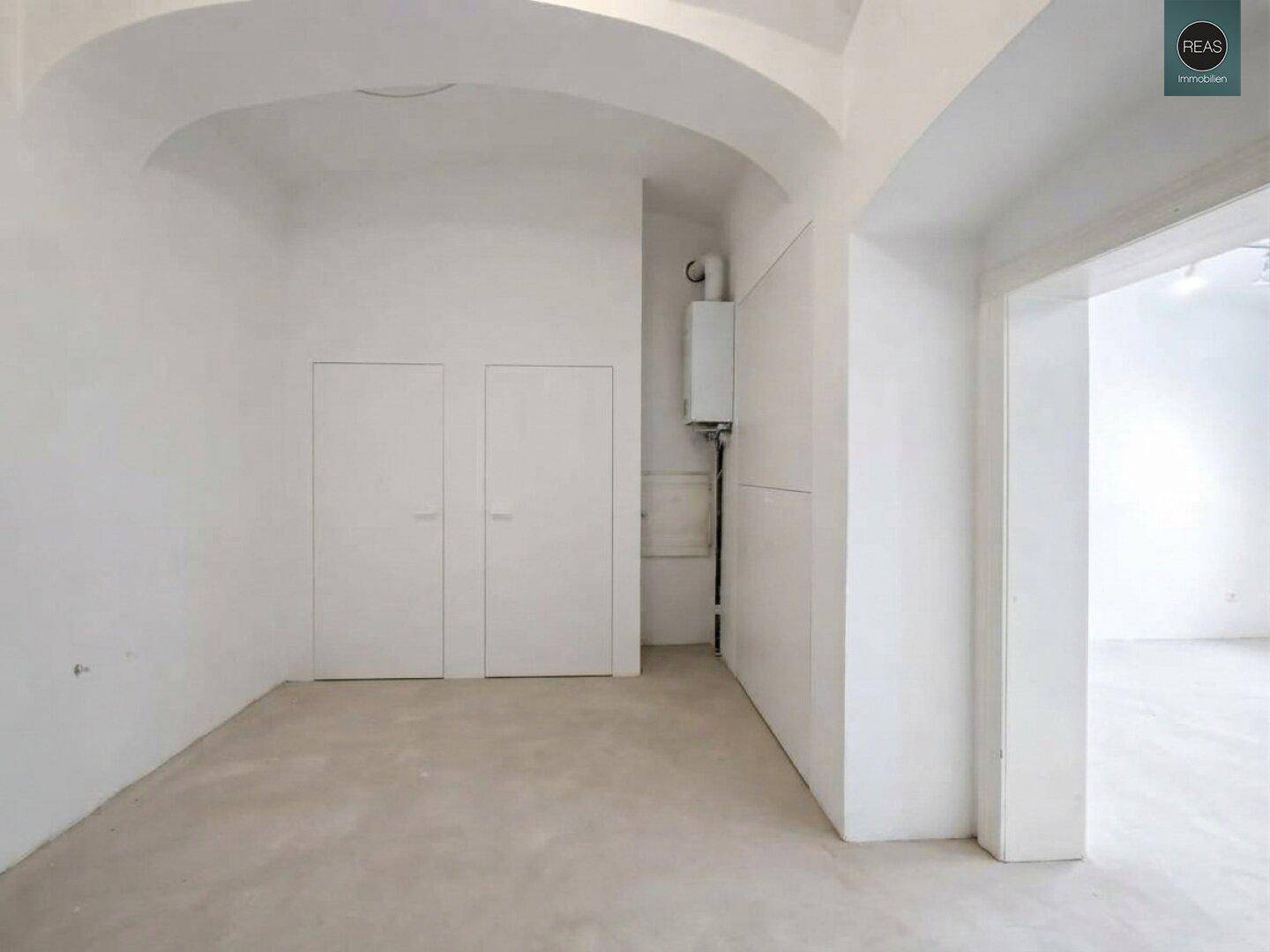Leerer Raum mit weiß gestrichenen Wänden, Einbauschränken und einem Heizkessel an der Wand.
