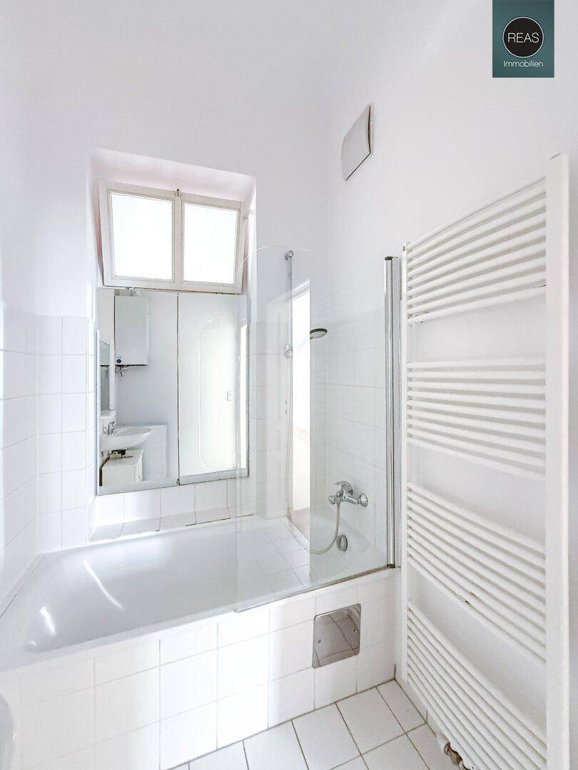 Modernes Badezimmer mit Badewanne, Duschabtrennung und Handtuchheizkörper, hell gefliest.