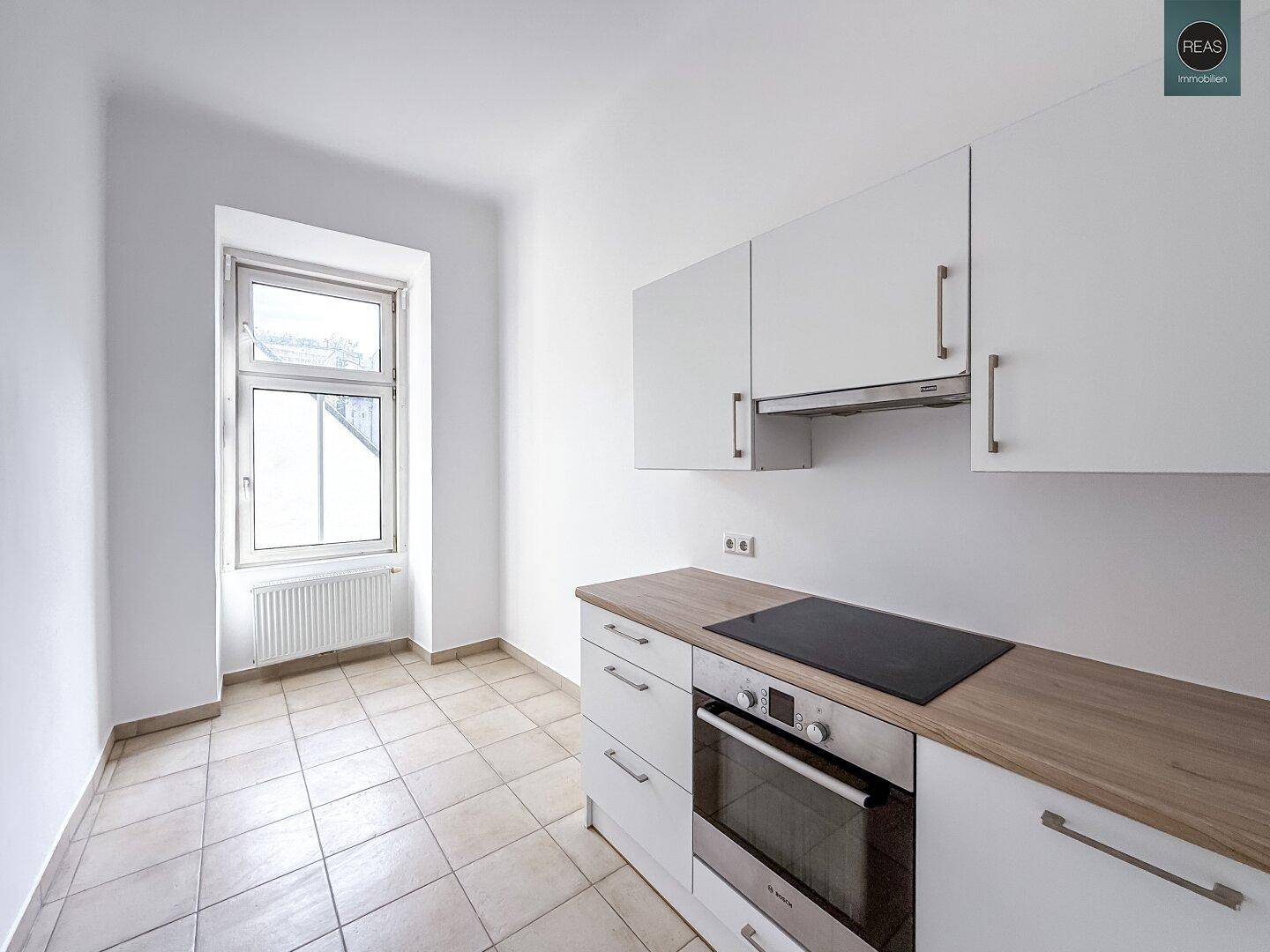 Moderne Küche mit weißen Schränken, Holzarbeitsplatte und integriertem Kochfeld und Backofen.