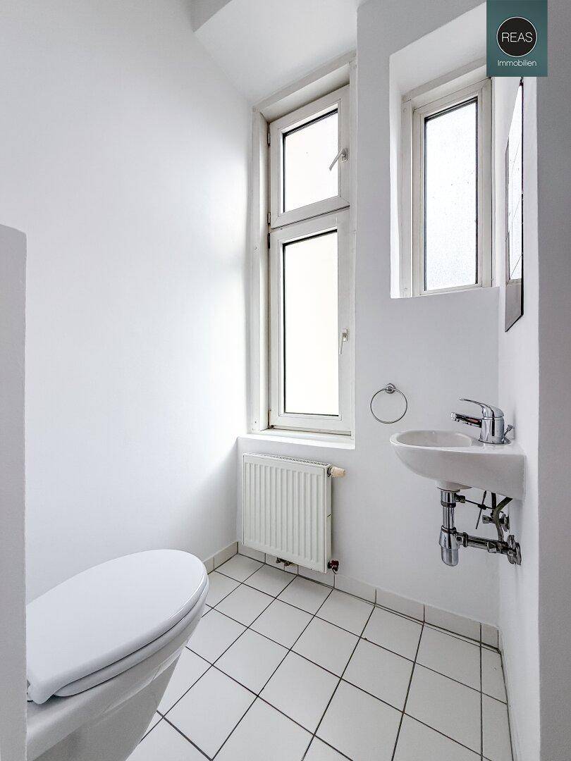 Separate Gästetoilette mit WC, kleinem Waschbecken und Fenster, weiß gefliest.