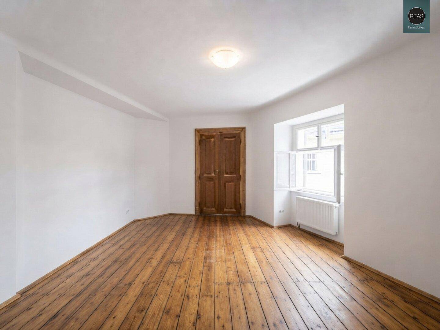 Helles Zimmer mit breiten Holzplanken und einem großen Fenster, das viel Tageslicht bietet.