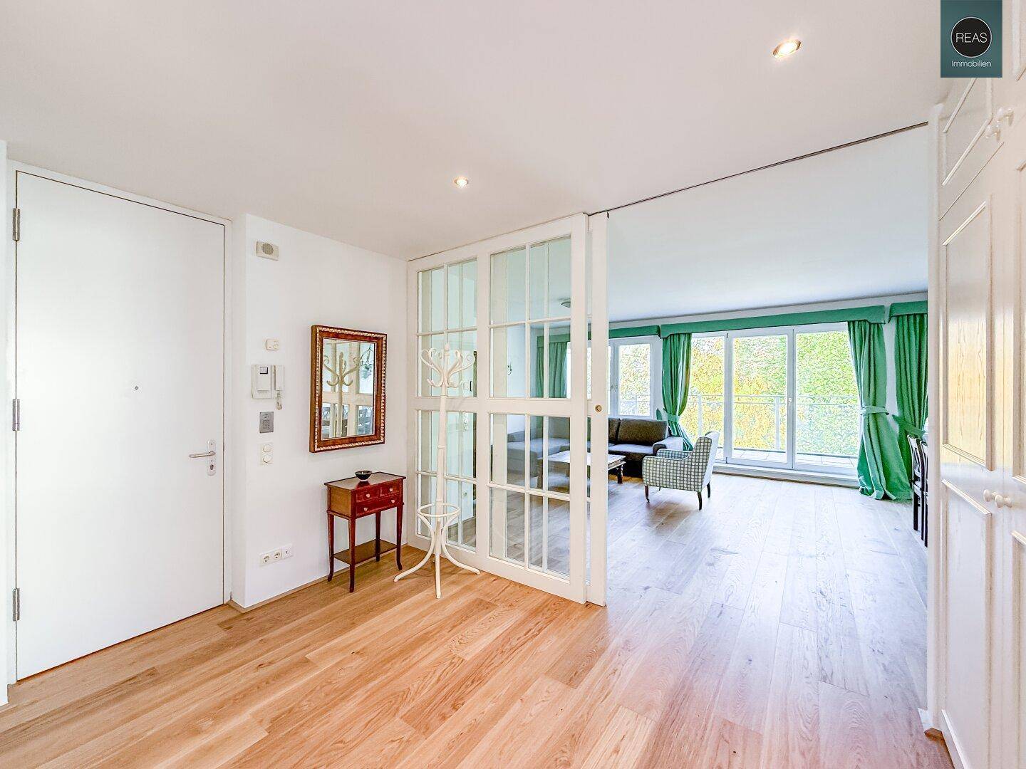 Heller Eingangsbereich mit Holzboden und Glastüren, der in ein Wohnzimmer führt.