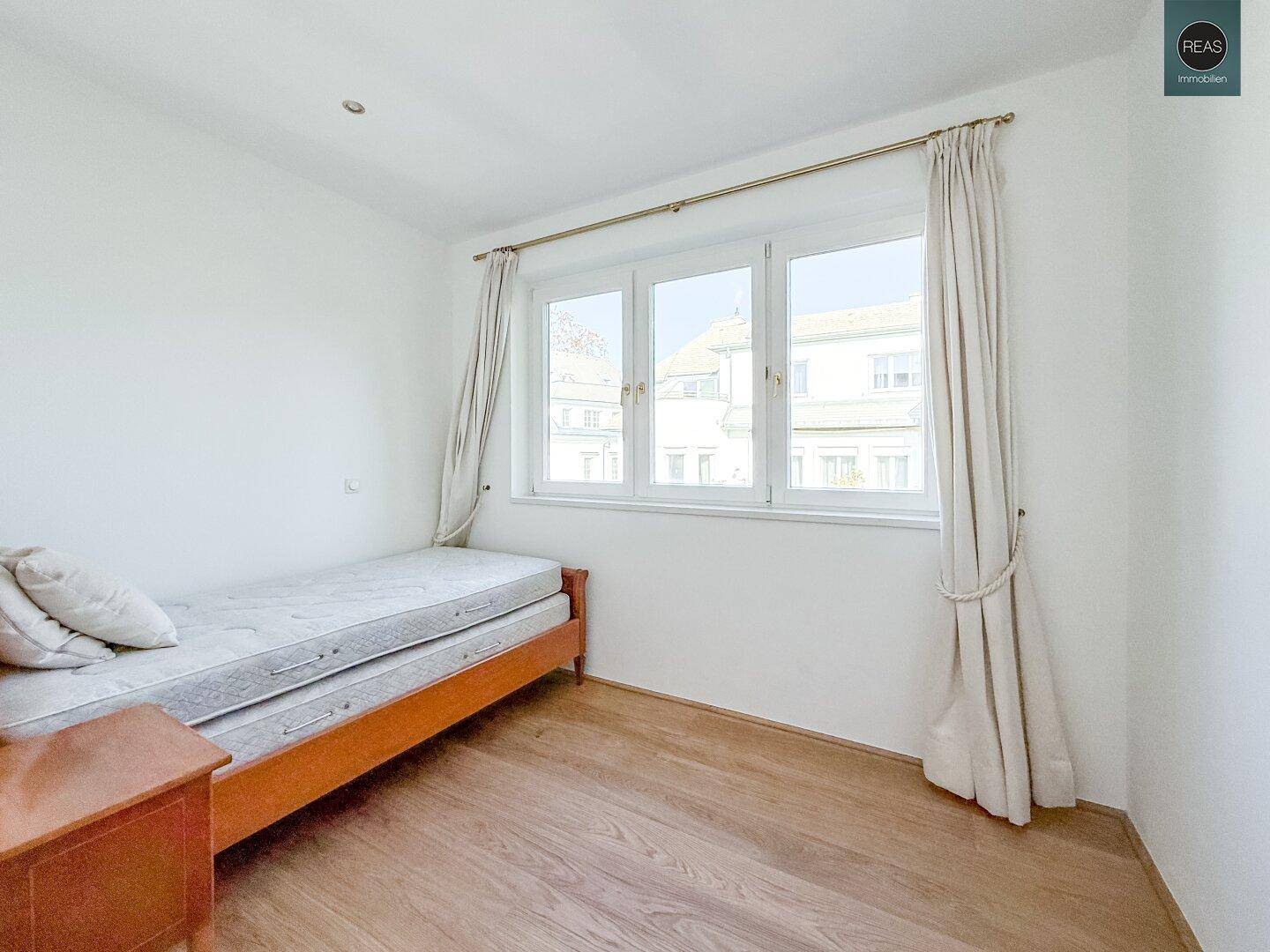 Helles Schlafzimmer mit Holzboden, Einzelbett und großem Fenster mit Blick nach draußen.