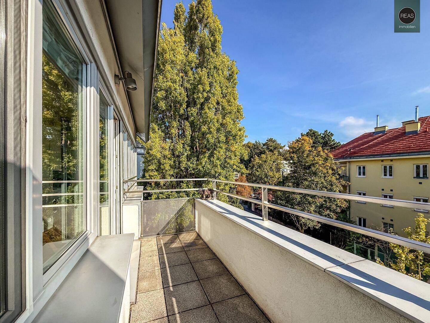 Schmaler Balkon mit Fliesenboden und Blick auf Bäume und die umliegenden Gebäude.