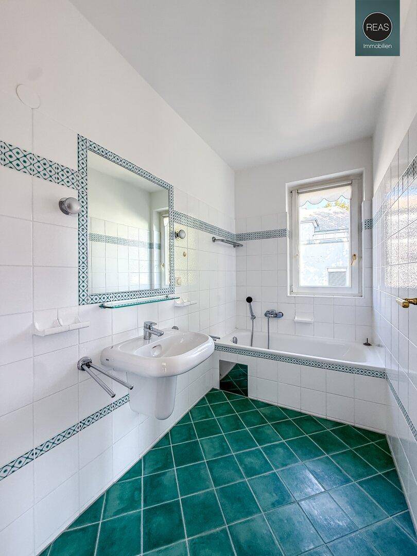 Badezimmer mit Badewanne, Waschbecken und grünen Fliesen im Retro-Stil der 80er Jahre.