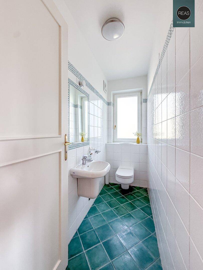 Separate Toilette mit Waschbecken, Fenster und grünen Bodenfliesen im Vintage-Stil.