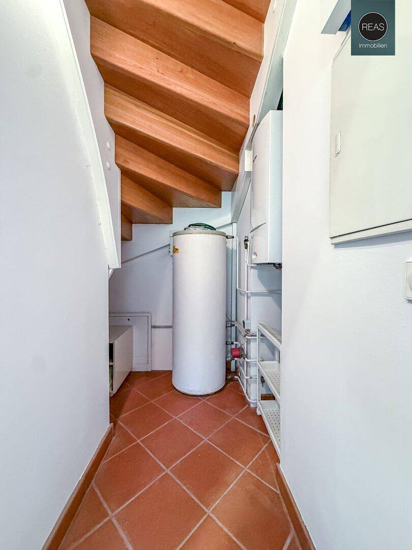 Praktischer Hauswirtschaftsraum unter der Holztreppe mit Warmwasserspeicher und Regalen.