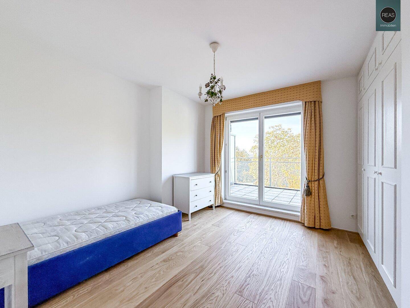 Helles Schlafzimmer mit Einzelbett, Parkettboden und Zugang zu einem Balkon.