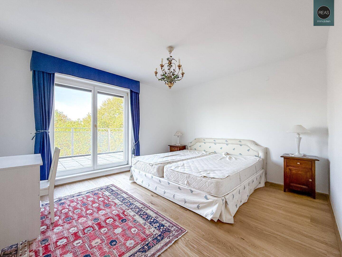 Schlafzimmer mit Doppelbett, Parkettboden und Zugang zu einem Balkon mit grüner Aussicht.
