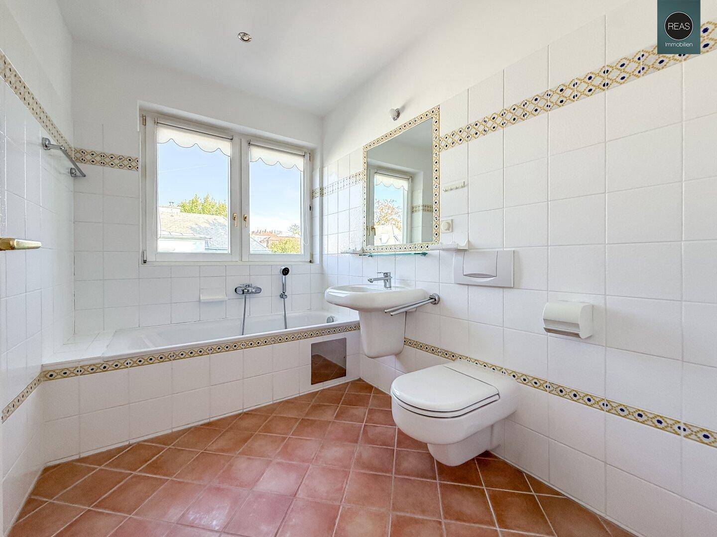 Badezimmer mit Badewanne, Waschbecken, Toilette und Fenster, hell gefliest.