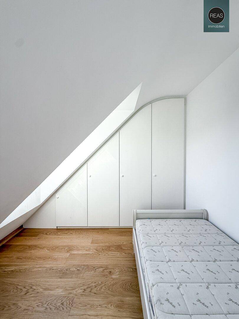 Schlafzimmer im Dachgeschoss mit Einzelbett, Einbauschränken unter der Dachschräge und Holzboden.