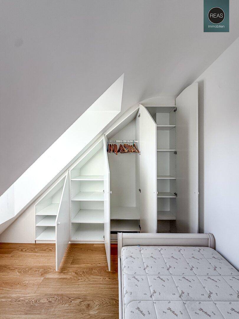 Geöffnete Einbauschränke im Dachgeschoss-Schlafzimmer mit praktischen Regalen und Kleiderstange.