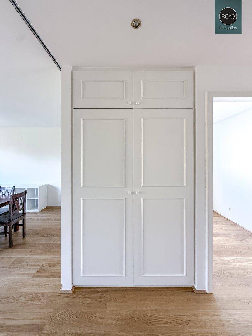 Klassischer Einbauschrank mit weißen Flügeltüren in einem Durchgangsbereich mit Holzboden.