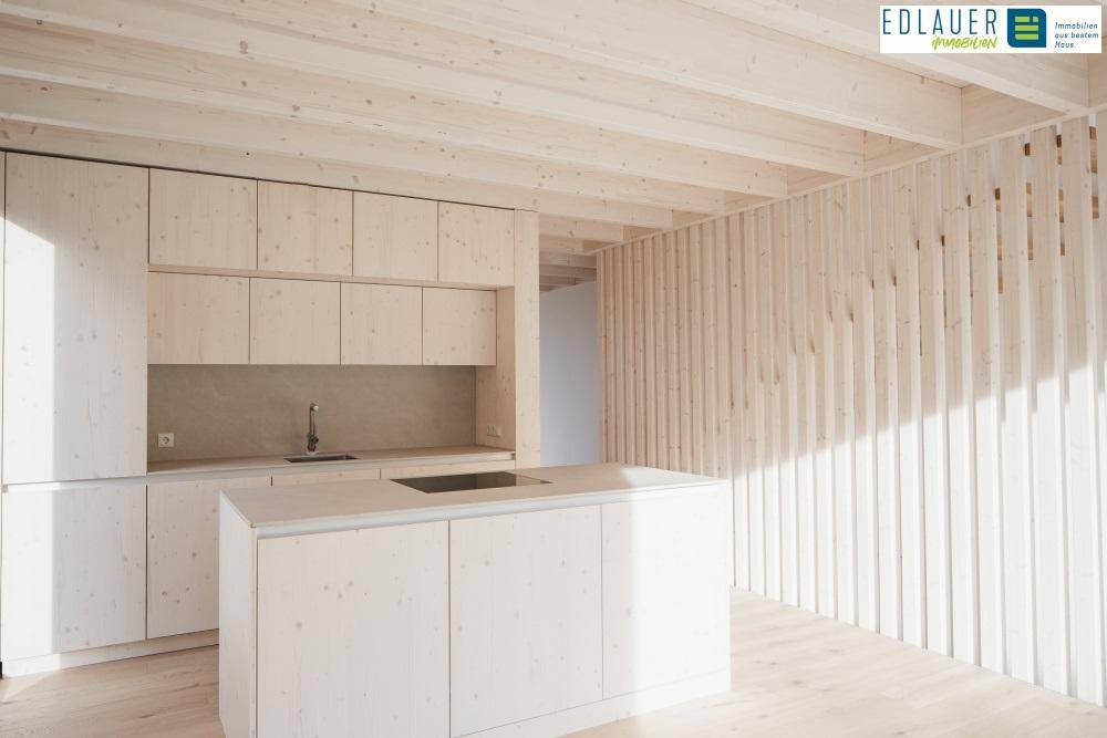 Moderne Küche mit hellen Holzschränken, Kücheninsel und sichtbaren Holzbalken an der Decke.